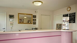 A reception desk with a pink counter, a mirror, framed certificates, and a clock on the wall.