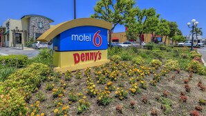A motel sign with 'motel 6' and 'Denny's' branding, surrounded by a landscaped garden with various plants and flowers. - Motel 6 Claremont, CA (Claremont)