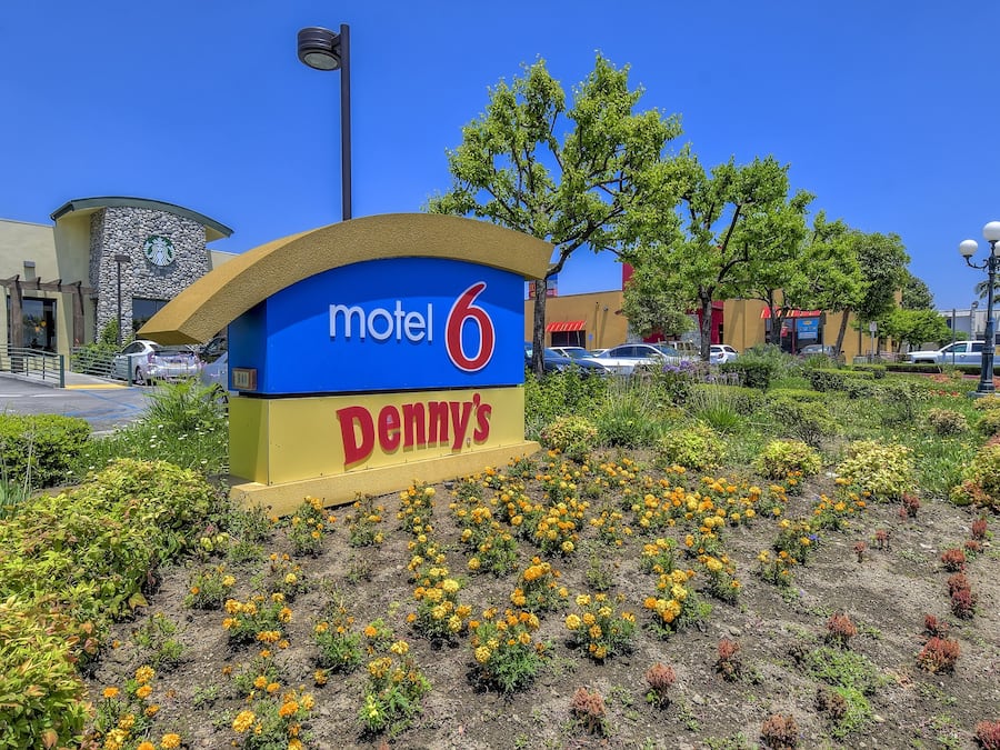 A motel sign with 'motel 6' and 'Denny's' branding, surrounded by a landscaped garden with various plants and flowers.