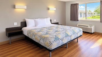 A hotel room with a bed, bedside tables, a window with curtains, and a wall-mounted air conditioner.