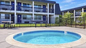 A swimming pool with a surrounding fence, a building with multiple balconies, and a small table with benches.