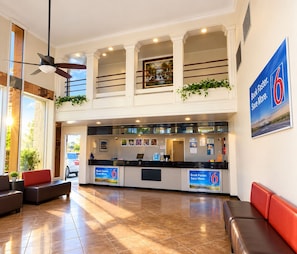 A hotel lobby with a reception desk, seating area, and a large window. - Motel 6 Claremont, CA (Claremont)