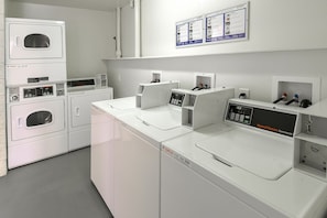 A commercial laundry facility with multiple washing machines and dryers, control panels, and instructional signage. - Motel 6 Claremont, CA (Claremont)