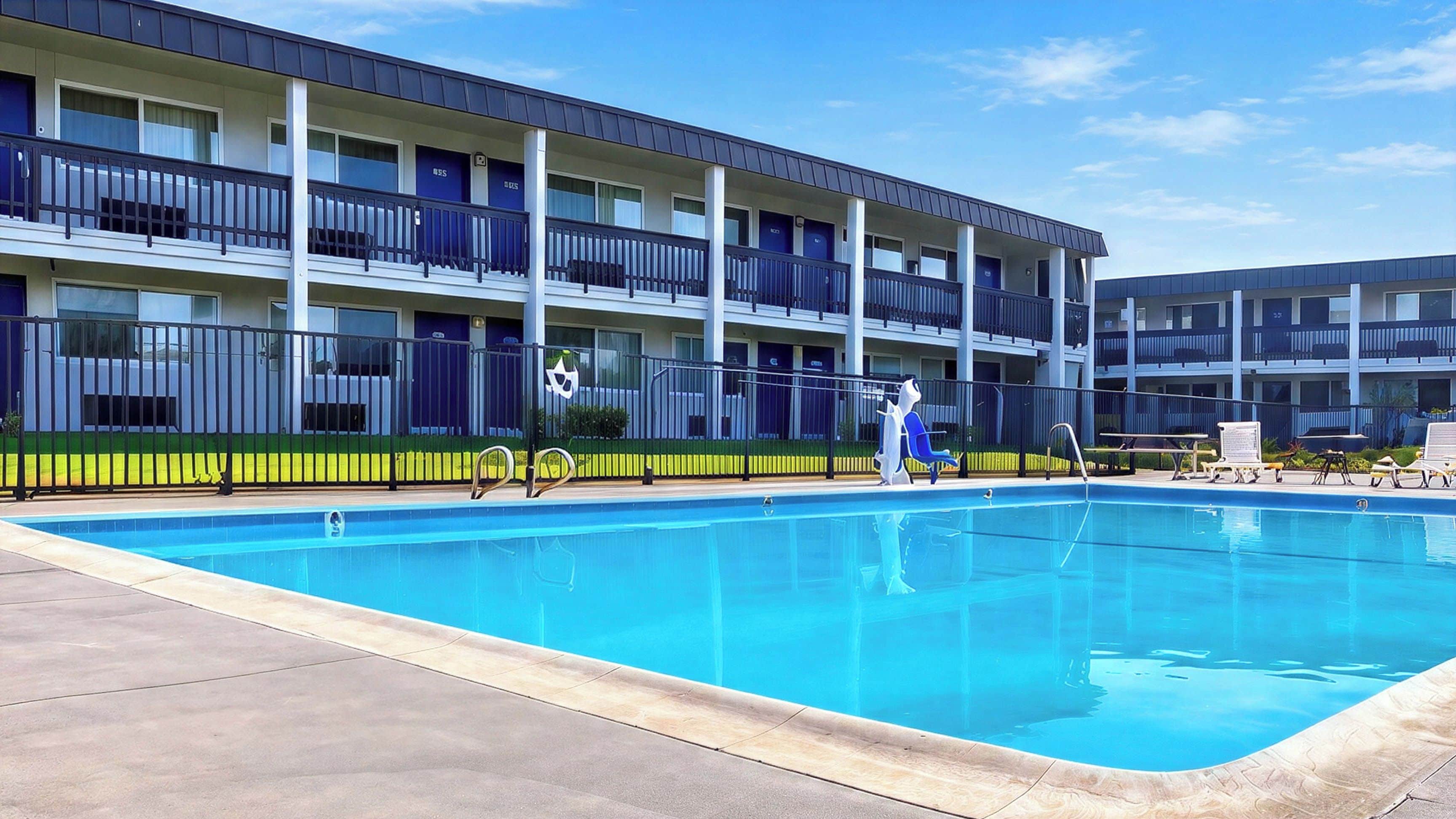A multi-story hotel with a swimming pool, balconies, and a clear sky.