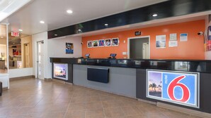 A hotel reception area with a black counter, orange walls, and a sign indicating room number 6. - Motel 6 Claremont, CA (Claremont)