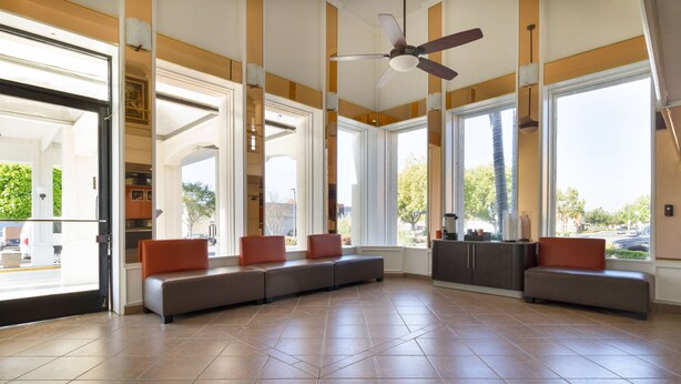 A spacious lobby with a long bench seating area, large windows, and a ceiling fan. - Motel 6 Claremont, CA (Claremont)