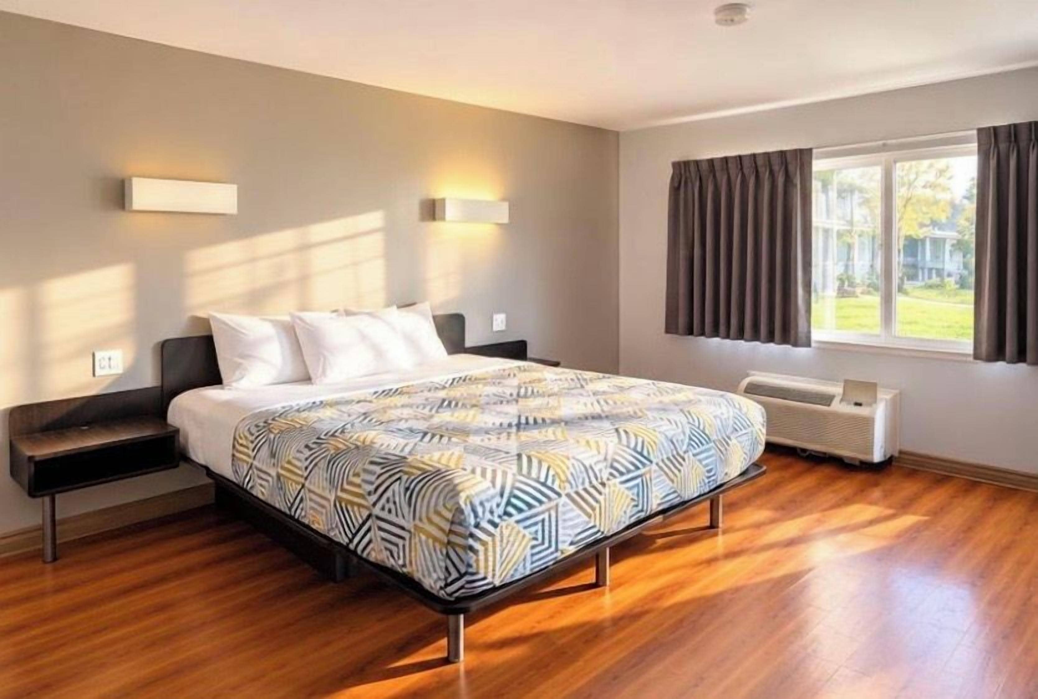 Une chambre à coucher comprenant un lit, des tables de chevet, une fenêtre avec des rideaux et un radiateur fixé au mur.