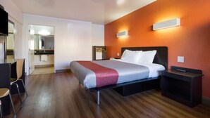 A modern hotel room with a bed, bedside table, and a small desk area. - Motel 6 Claremont, CA (Claremont)