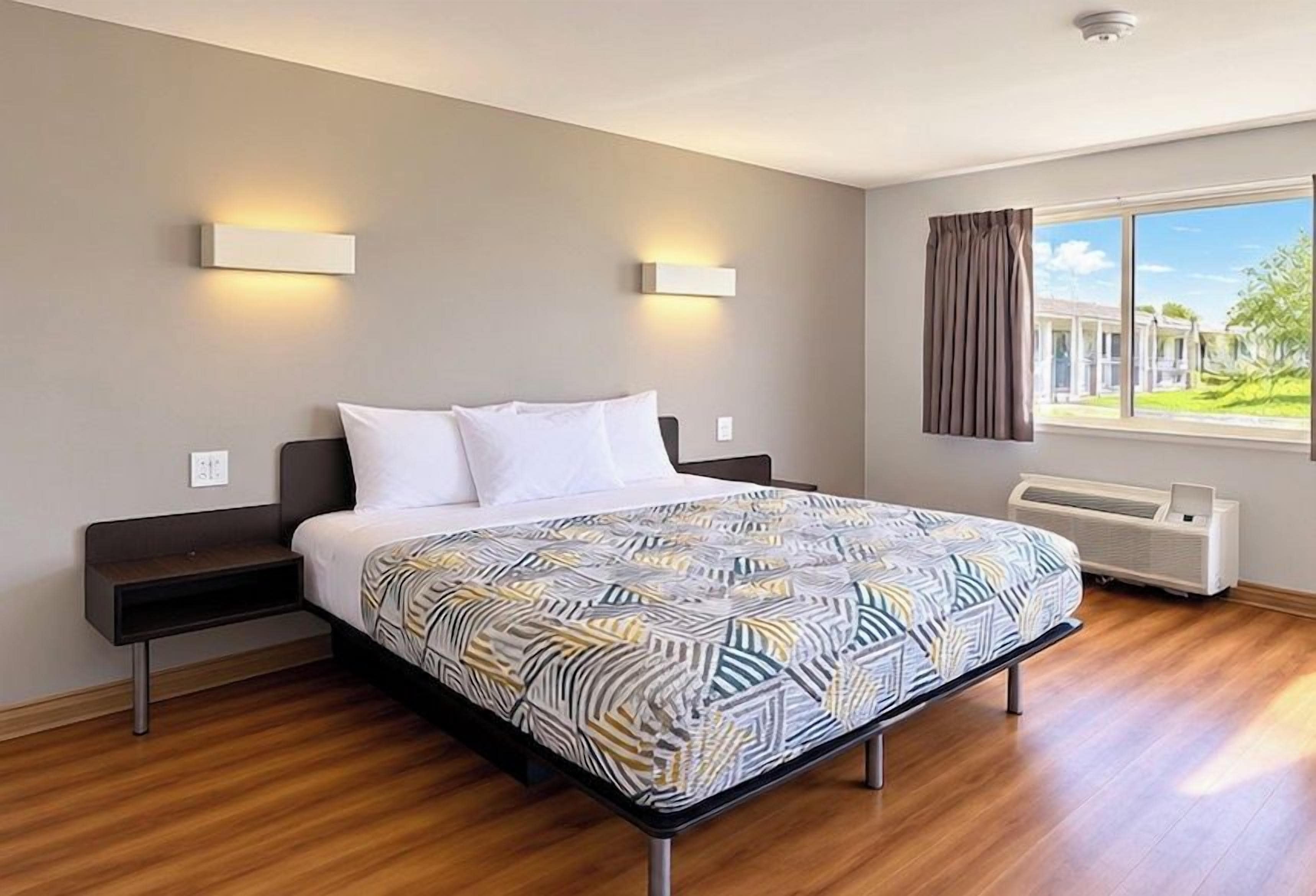 Ett modernt hotellrum med en stor säng, sängbord, ett fönster med gardiner och utsikt över omgivningen.