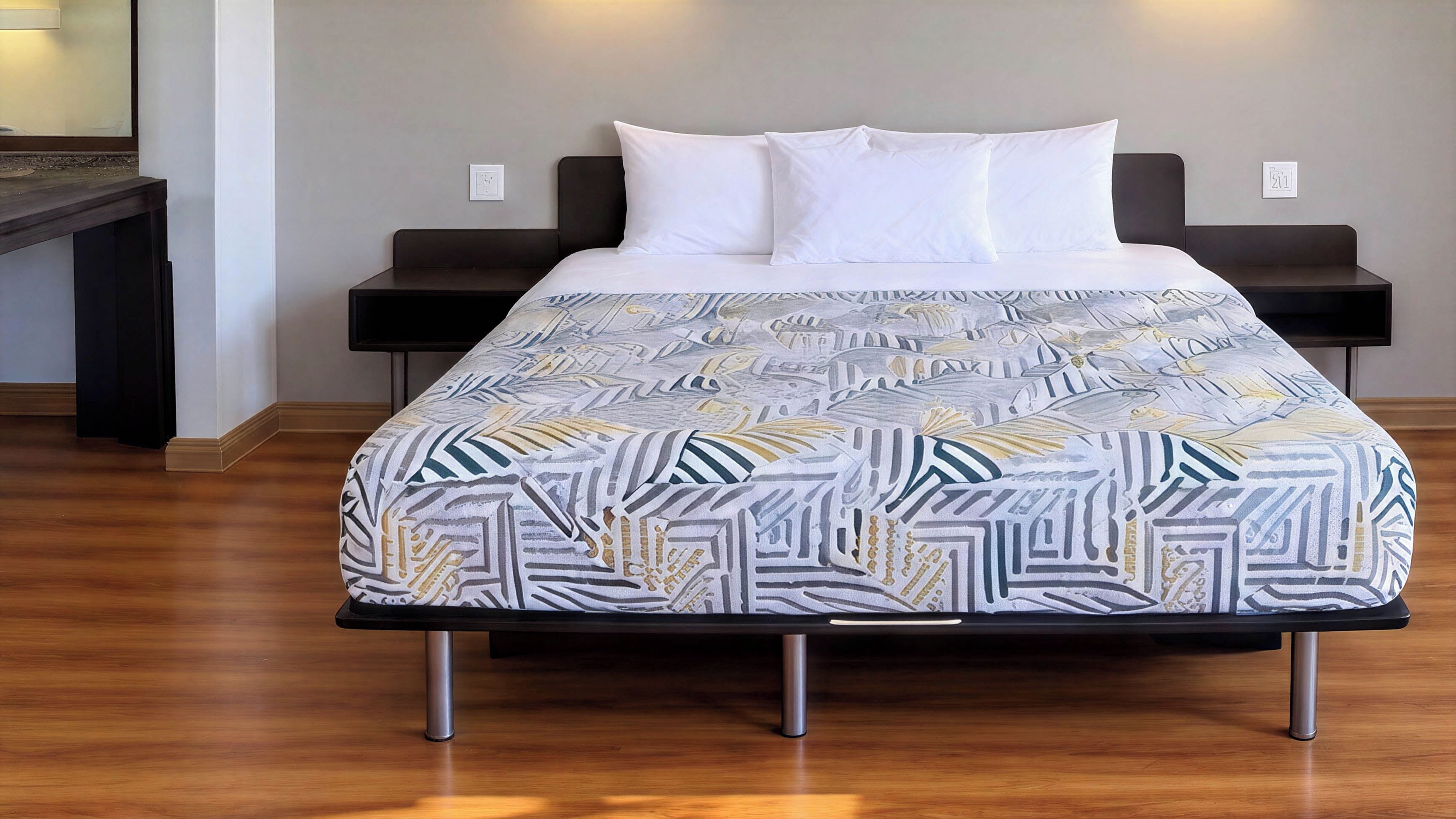 A bed with a patterned bedspread, two bedside tables, and a wooden floor.