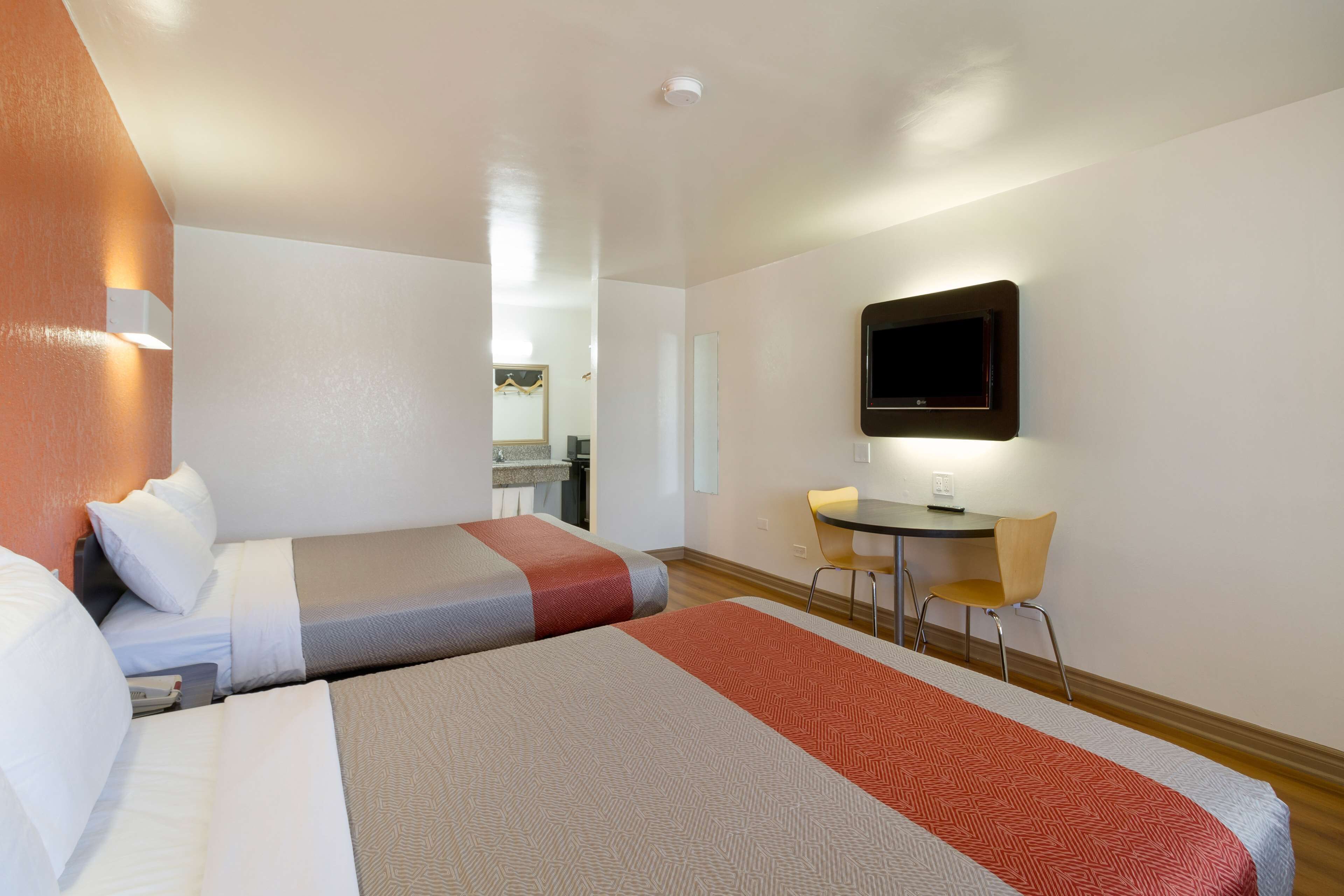 Habitación de hotel con dos camas, un escritorio, una silla y un televisor montado en la pared.