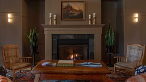 Un salon chaleureux avec une cheminée, deux fauteuils, une table basse avec des livres et un tableau au-dessus du manteau de la cheminée.