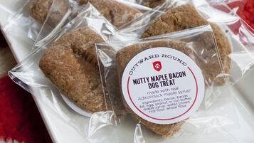 Ein Teller mit verpackten Hundeleckerlis, beschriftet mit 'Nutty Maple Bacon Dog Treat'. Die Zutatenliste enthält Speck, Ei, Erdnussbutter, Fett, Ei, Speck, Ahornsirup, Wasser, braunen Reismehl und Weizenmehl.