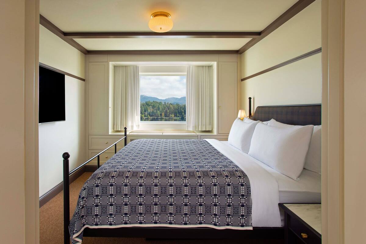 Une chambre d’hôtel avec un grand lit, une télévision, une fenêtre avec des rideaux et une vue sur une forêt.