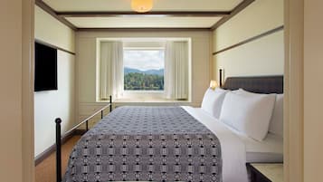 Habitación de hotel con una cama grande, televisión, ventana con cortinas y vista a un bosque.