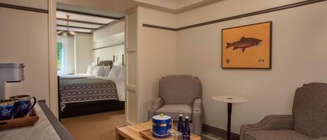 A hotel room with a bed, two armchairs, a coffee table with a tray of items, and a painting of a fish on the wall.
