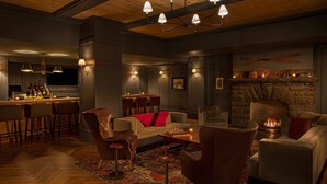 Un espace salon accueillant avec une cheminée en pierre, des fauteuils en cuir, un bar avec des tabourets et un éclairage d’ambiance.