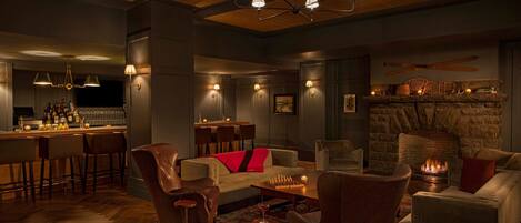 A cozy lounge area with a stone fireplace, leather armchairs, a bar with stools, and ambient lighting.