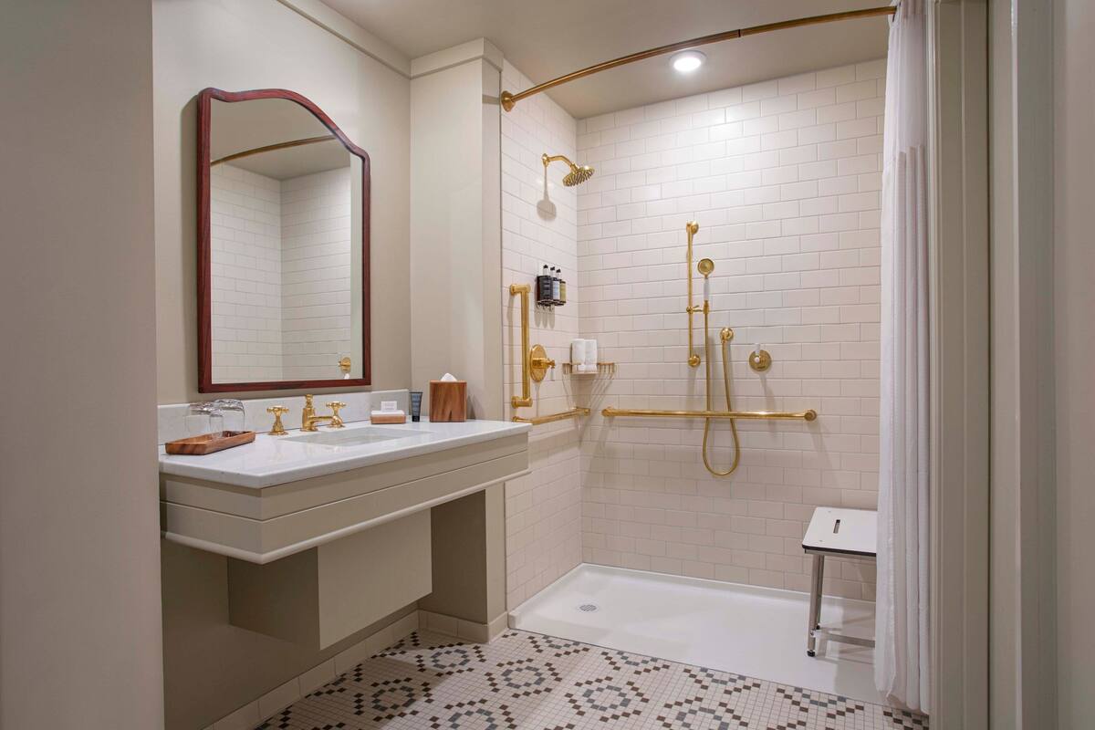 Une salle de bain moderne avec un lavabo blanc, des robinetteries dorées et une douche dotée d’une porte en verre.