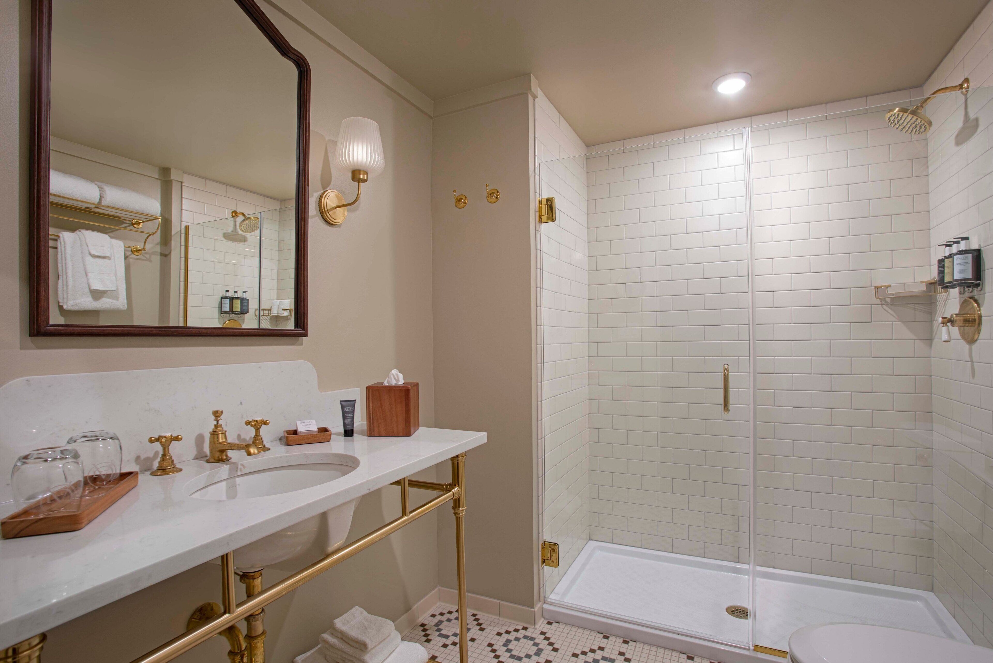 A bathroom with a white sink, gold fixtures, a glass-enclosed shower, and a mirror with wall sconces.