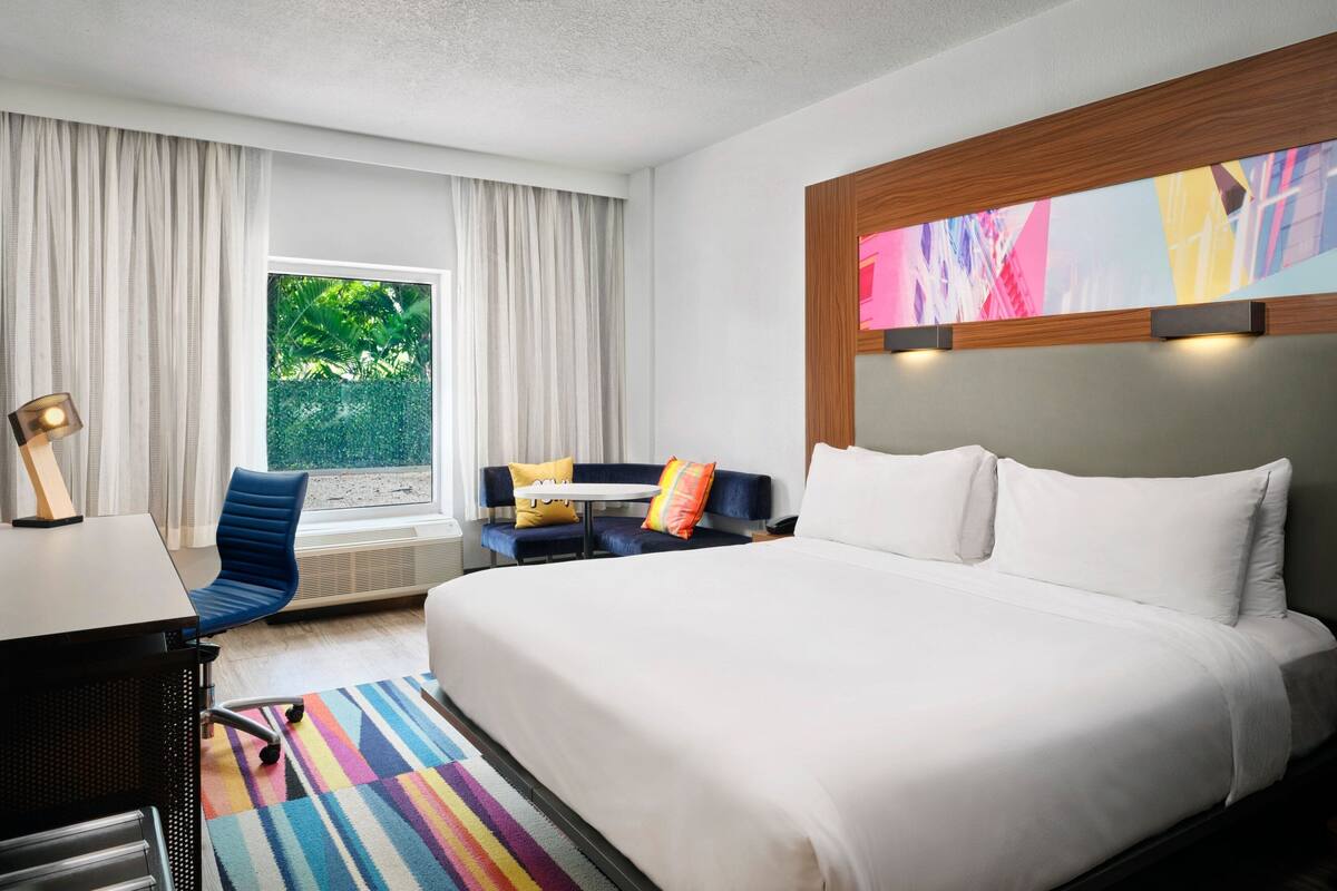 Ein Hotelzimmer mit einem großen Bett, einem Schreibtisch, einem Sessel und einer Couch, sowie einem Fenster mit Vorhängen.