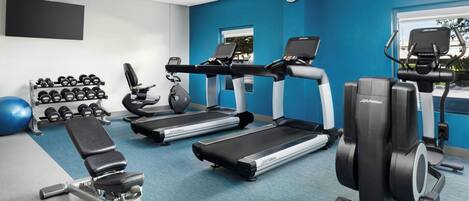 Un gimnasio con cintas de correr, mancuernas y un banco.