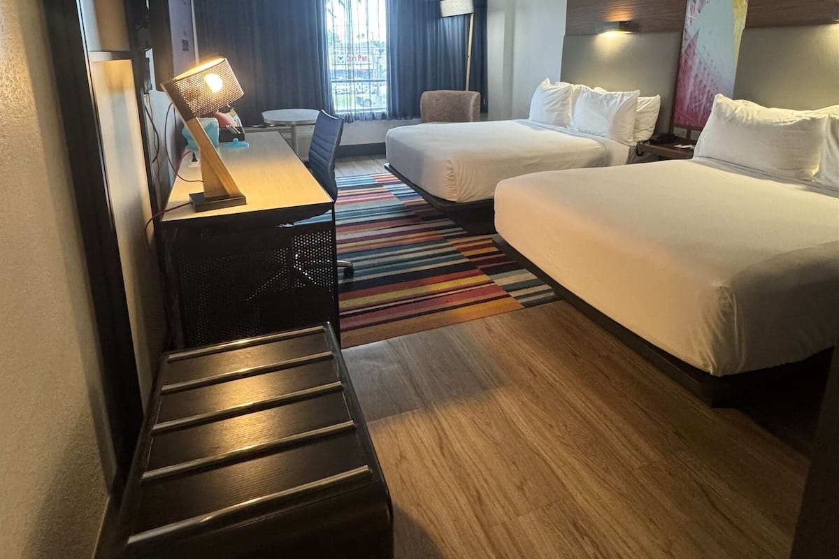 Ein Hotelzimmer mit zwei Betten, einem Schreibtisch, einem Stuhl, einer Lampe und Blick ins Freie.