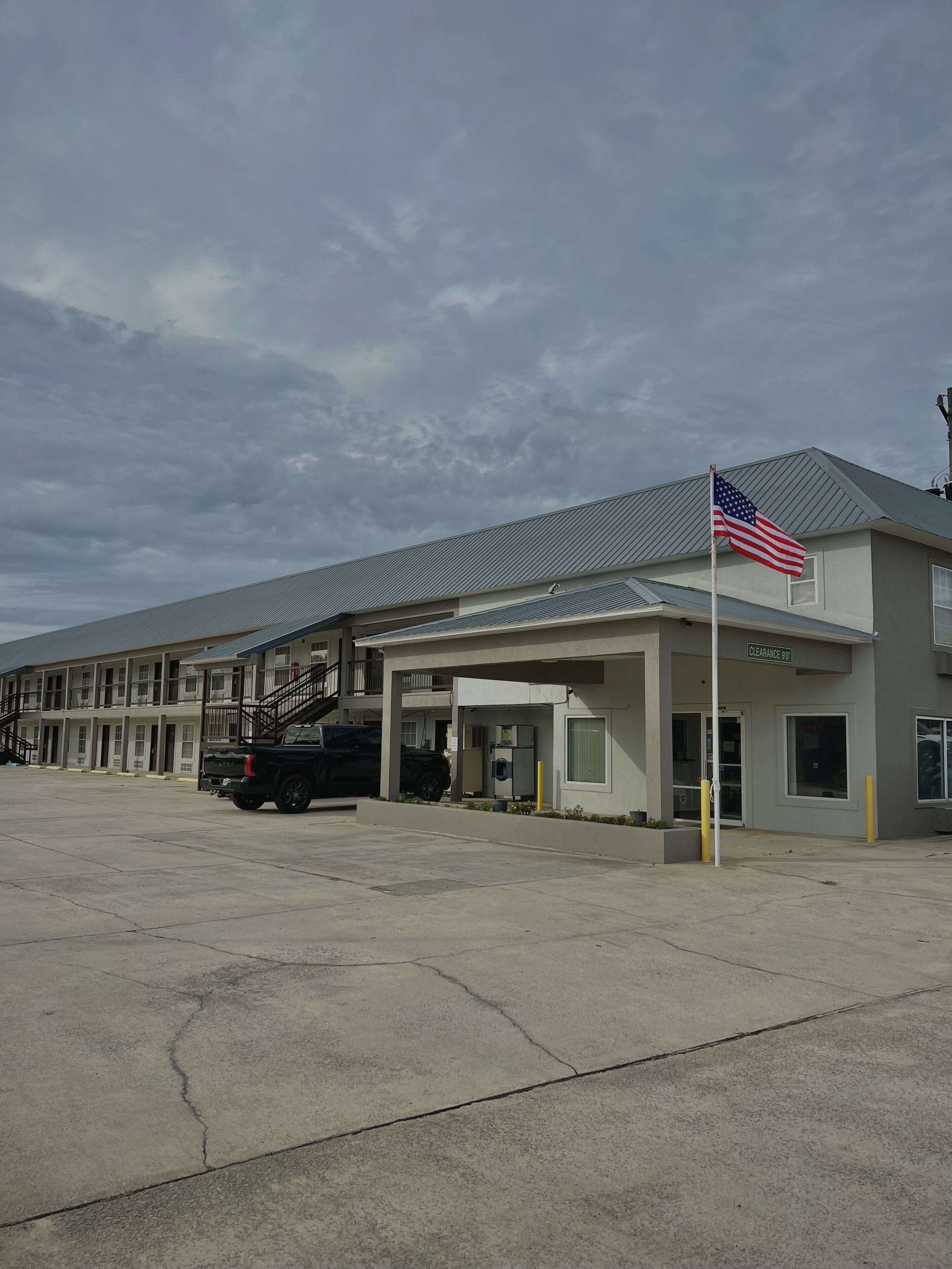 A motel with a parking lot, a black truck, and an American flag.