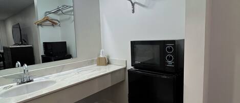 A modern bathroom with a large mirror, a sink, a black refrigerator, and a towel rack.