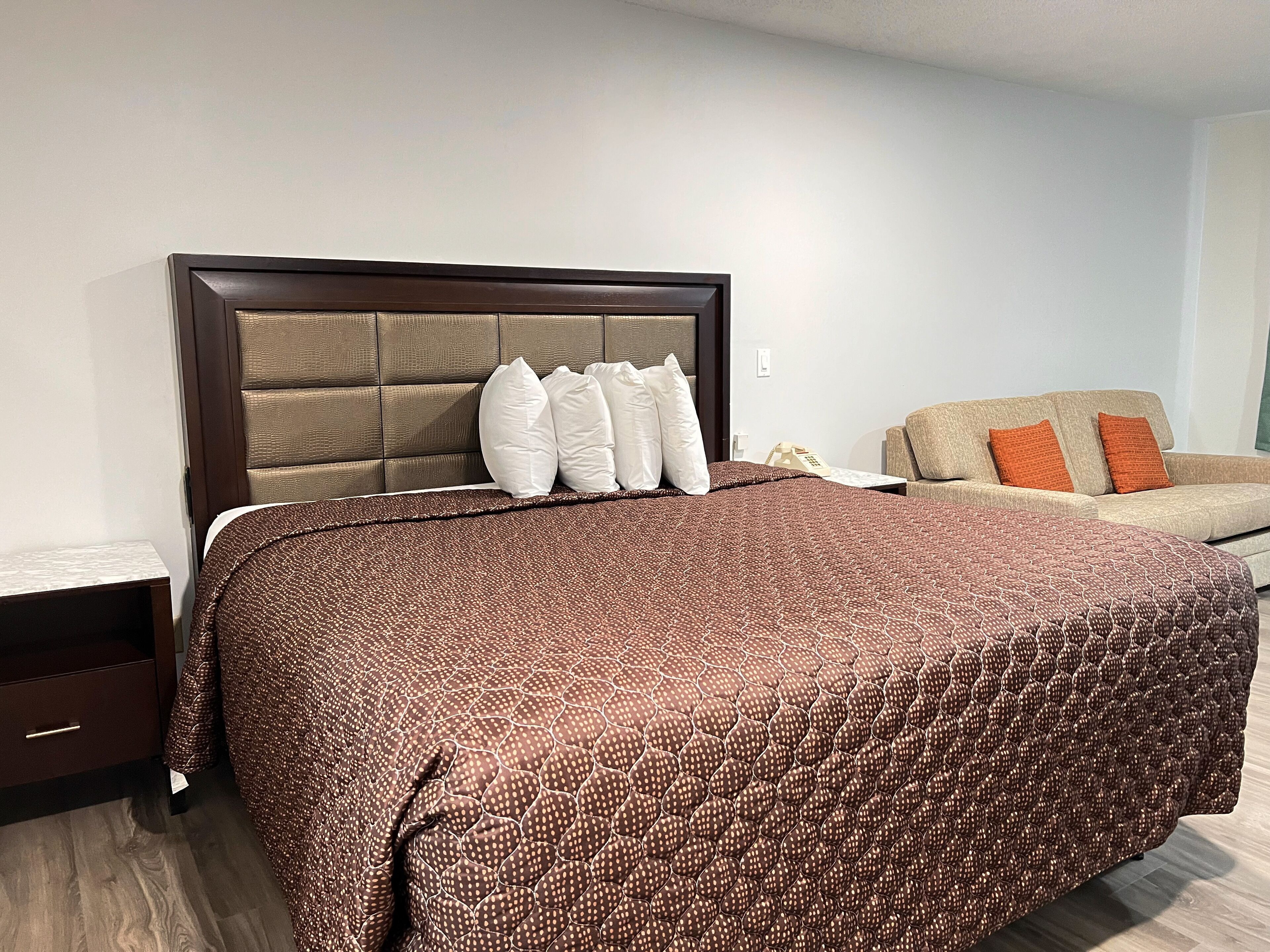 A bedroom with a large bed, a nightstand, a sofa, and a headboard.