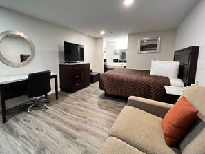 A hotel room with a bed, a desk with a chair, a dresser, a television, and a large mirror. - Garden Inn & Suites (Metter)