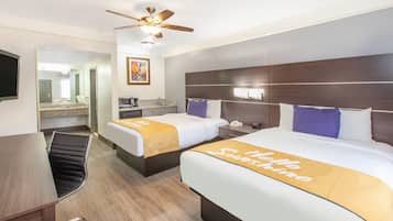 Habitación de hotel con dos camas, un escritorio, una silla, ventilador de techo, microondas y un cuadro en la pared.