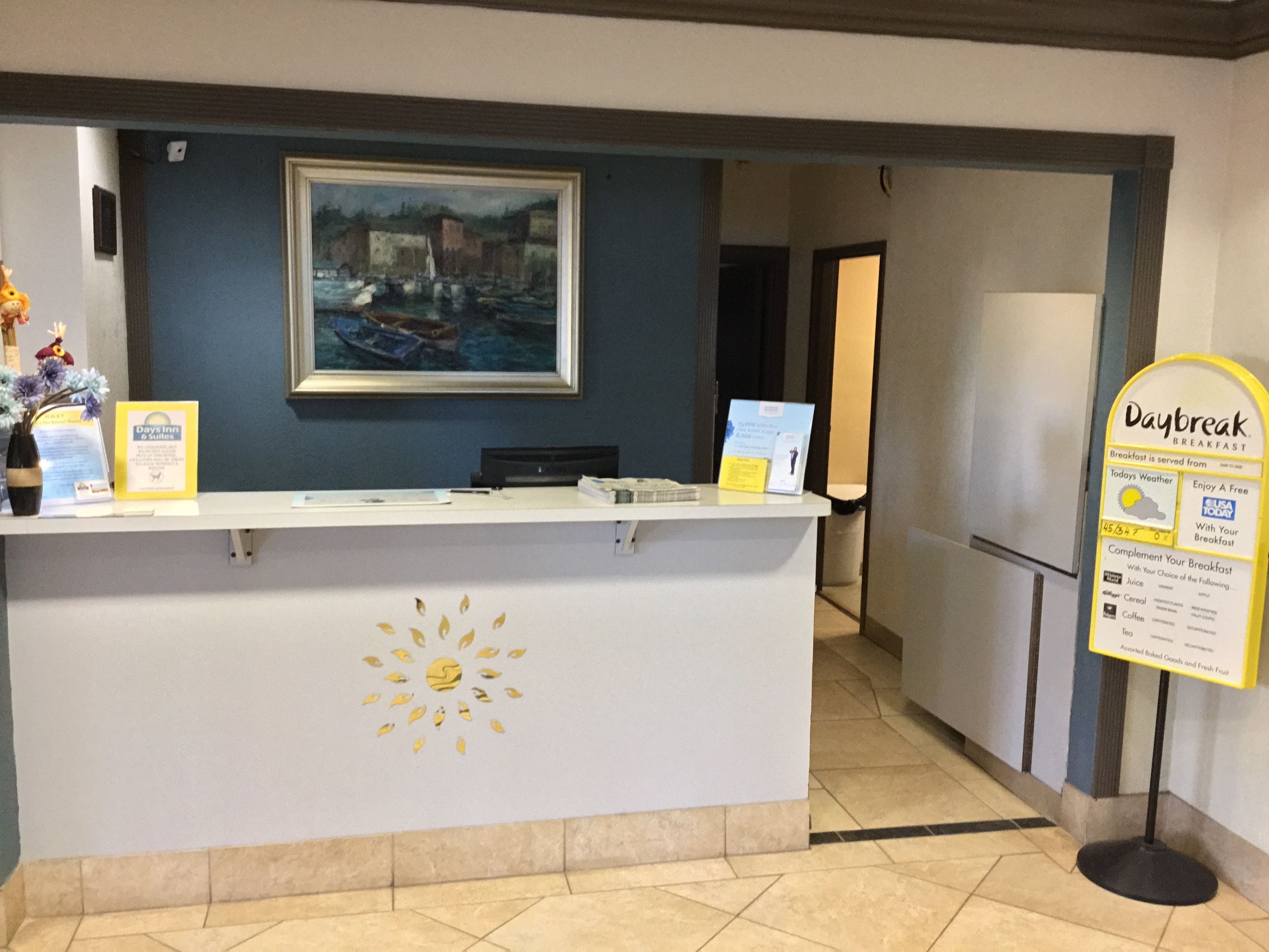 A reception desk with a framed painting above it, a sign for Daybreak Breakfast, and a sun design on the desk.
