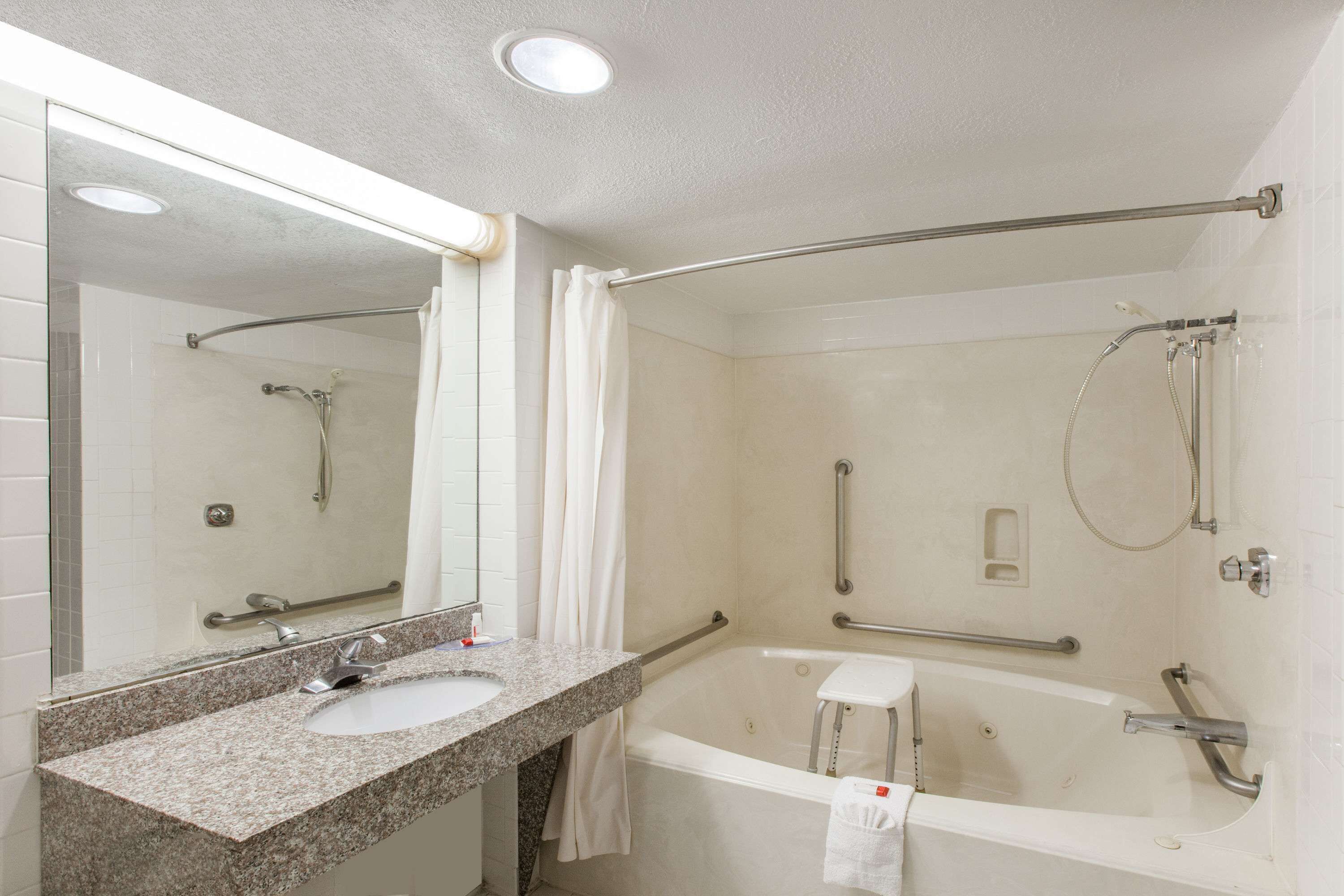 A modern bathroom with a granite sink, a bathtub, a shower with a handheld showerhead, and a glass-enclosed shower stall.