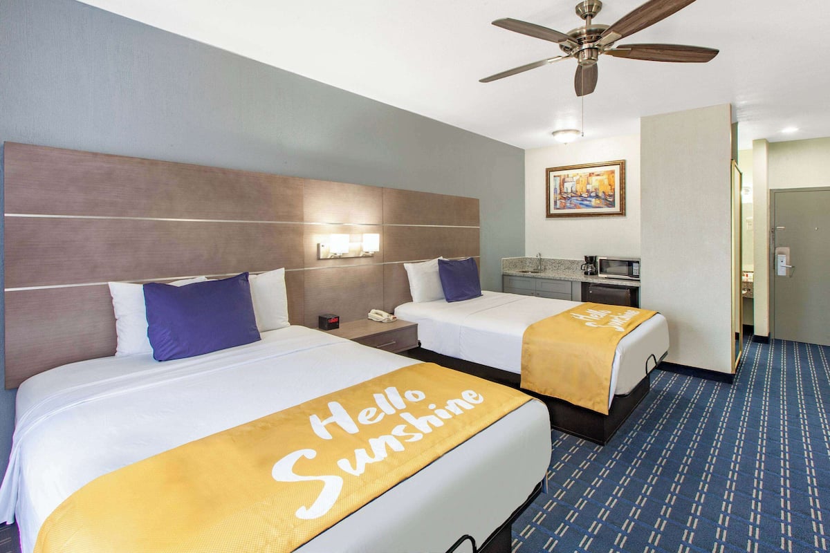 A hotel room with two beds, a ceiling fan, a nightstand with a phone, a microwave, and a painting on the wall.