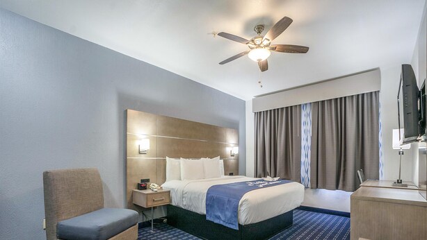 Hotelkamer met een bed, stoel, bureau, plafondventilator en een televisie.