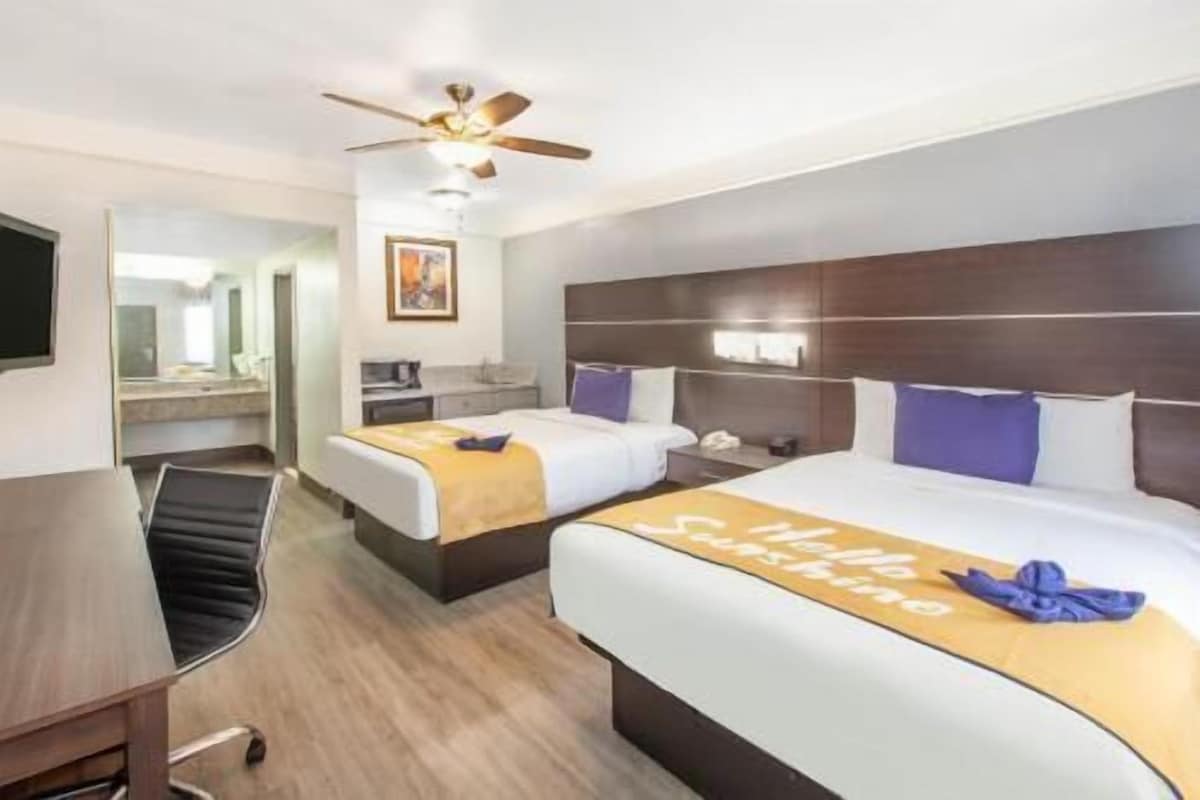 A hotel room with two beds, a desk, a chair, a ceiling fan, and a bathroom visible through an open door.