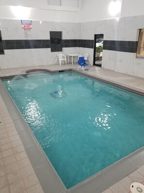 An indoor swimming pool with clear water, white and black tiled walls, and a sign warning of no lifeguard on duty. - Days Inn & Suites by Wyndham Webster NASA-ClearLake-Houston (Webster)