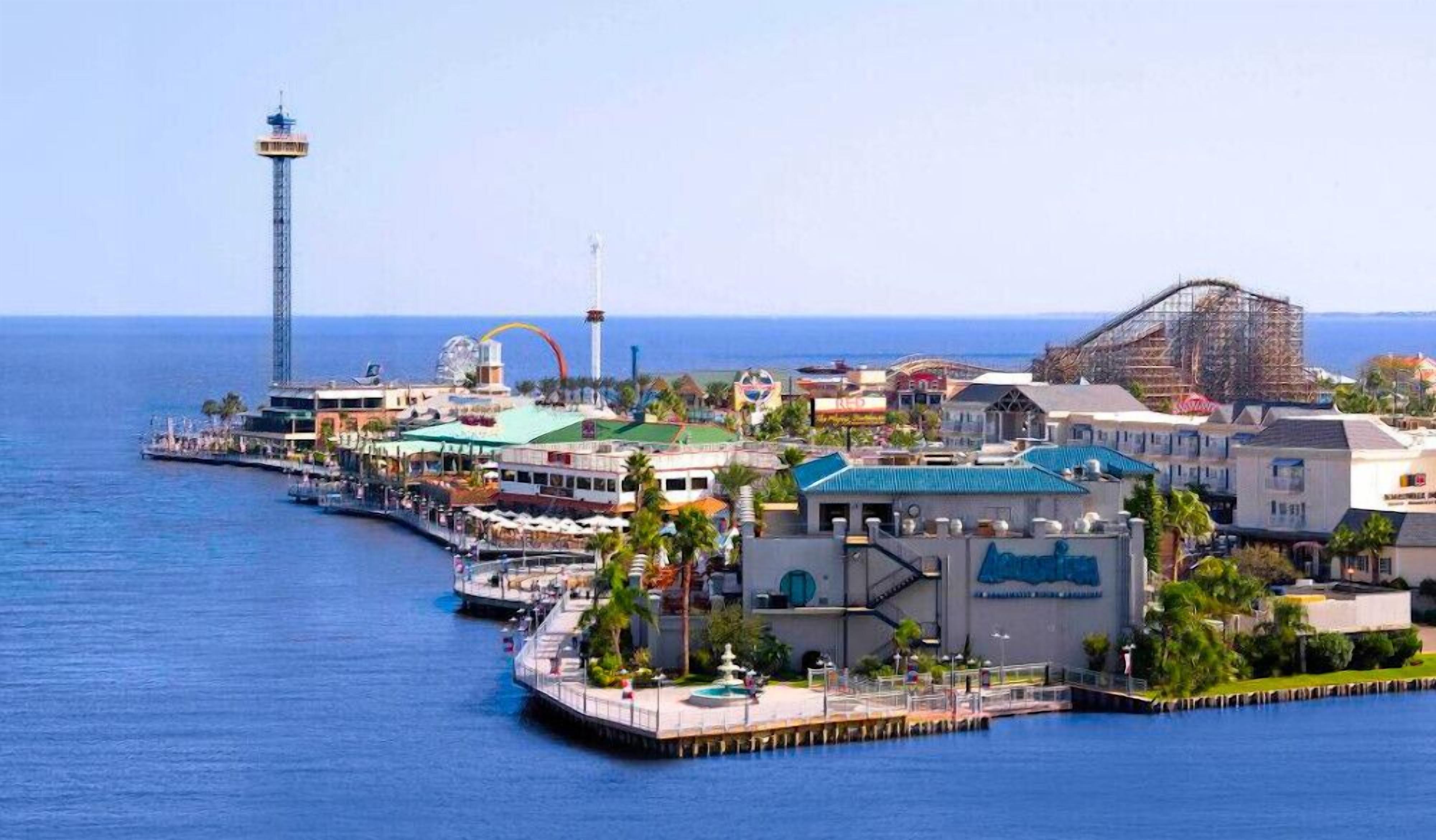 A coastal town with a prominent lighthouse, a pier with boats, and a variety of buildings including a large structure with a blue roof.
