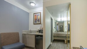 Een compacte hotelkamer met een kitchenette, een zithoek en een badkamer met spiegel.
