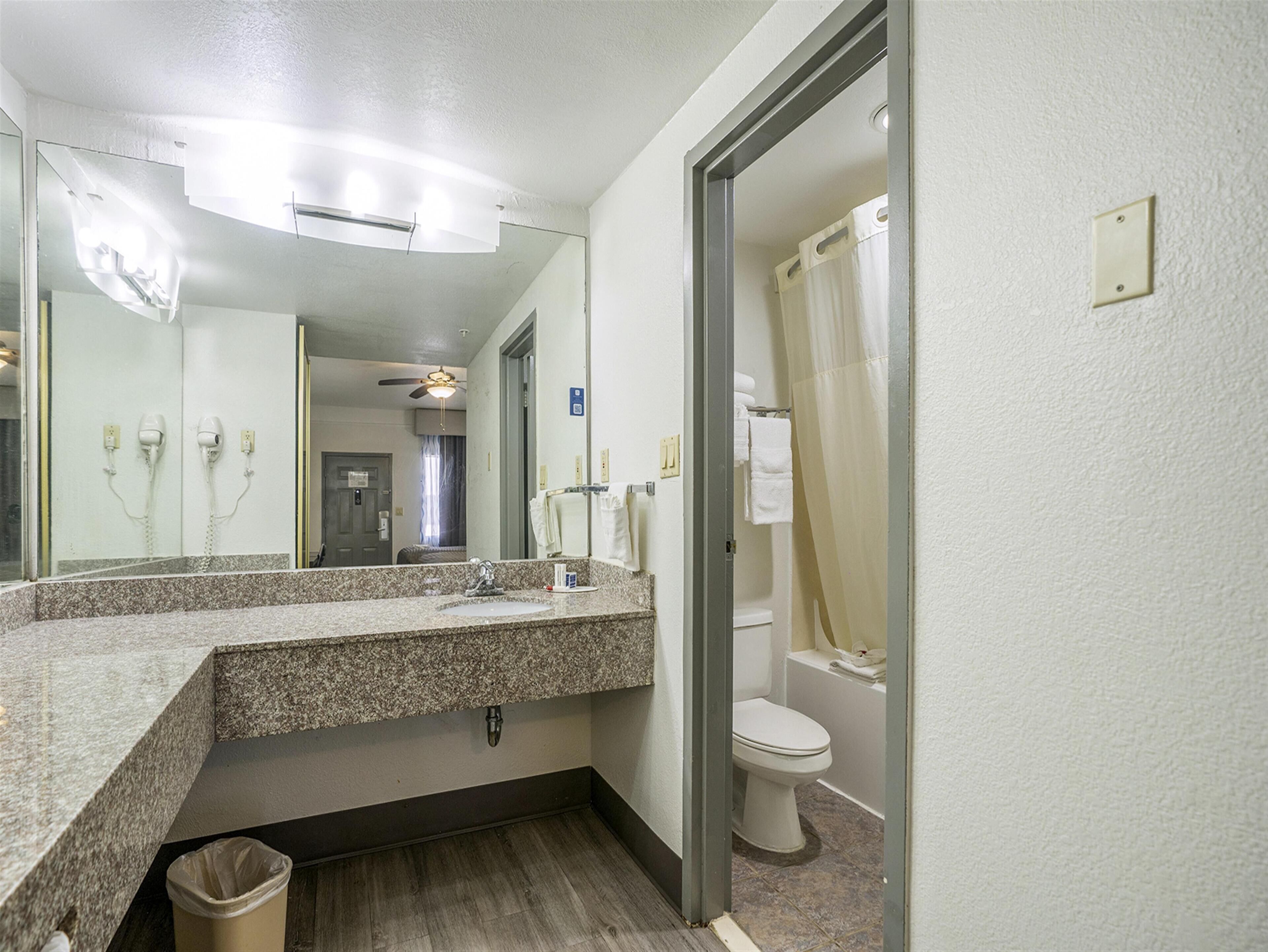 A bathroom with a granite countertop sink, a mirror, a ceiling fan, and a toilet.