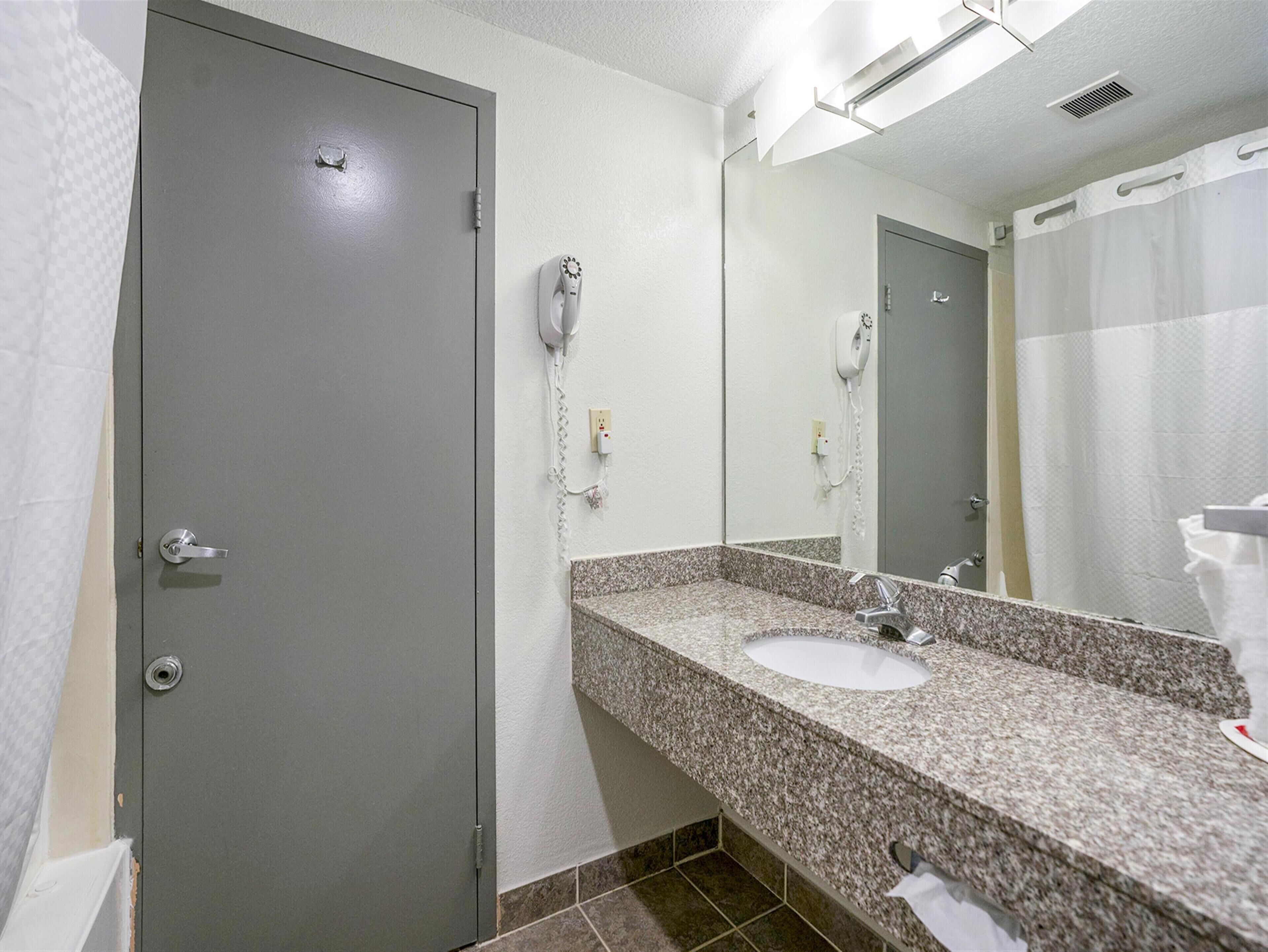 A bathroom with a granite countertop sink, a mirror, a hairdryer, and a shower curtain.