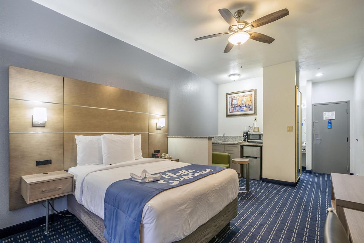 A hotel room with a bed, bedside tables, a desk, a kitchenette, and a ceiling fan.