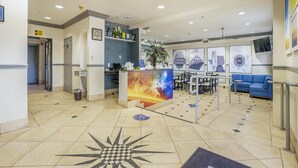 Een hotellobby met een receptiebalie, een zithoek en ingelijste foto’s aan de muur.