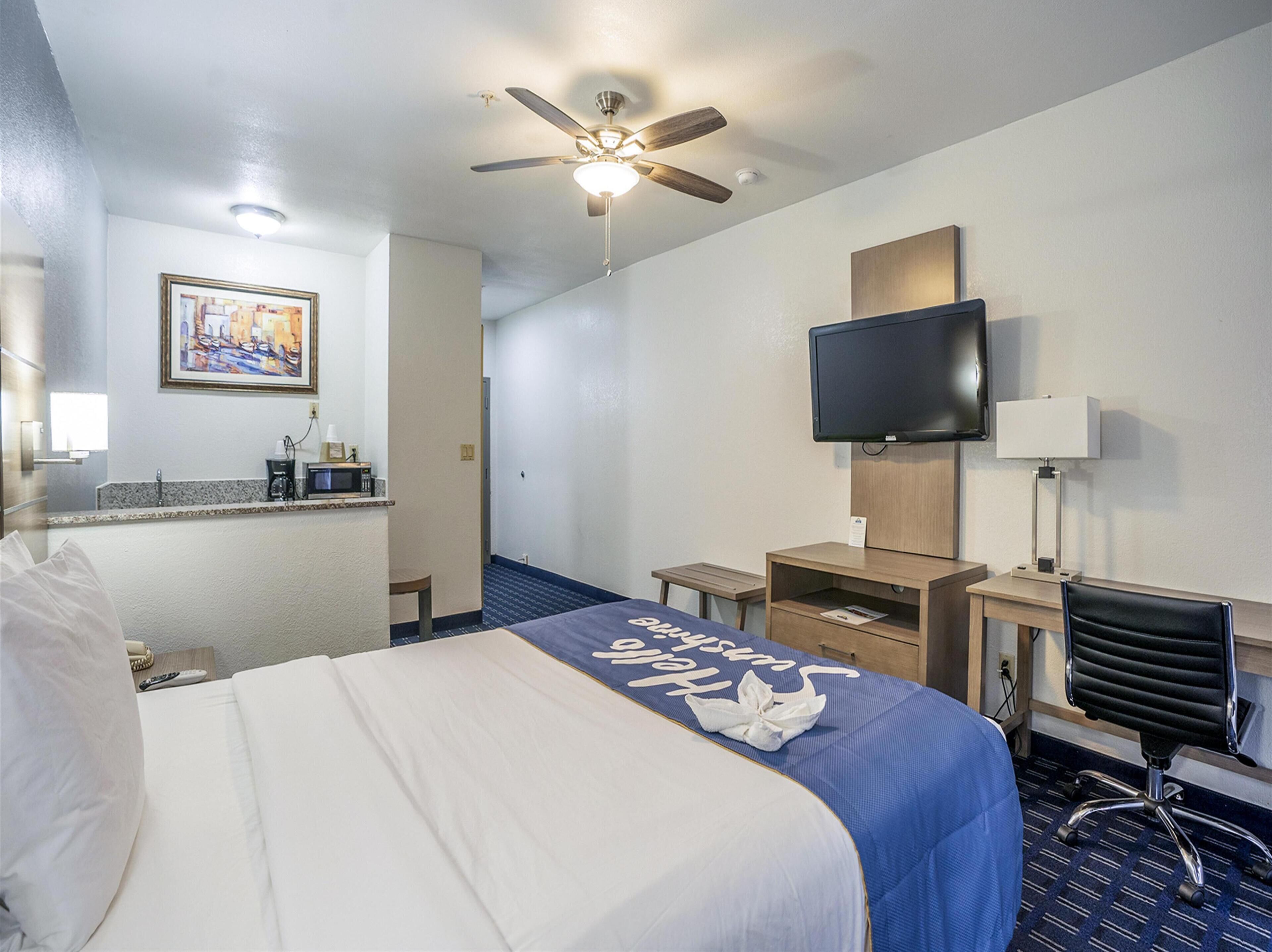 A hotel room with a bed, a desk, a chair, a television, and a ceiling fan.