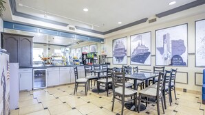 Een restaurant met betegelde vloer, tafels, stoelen, een balie met een koffieapparaat en lijstjes met foto's aan de muur.