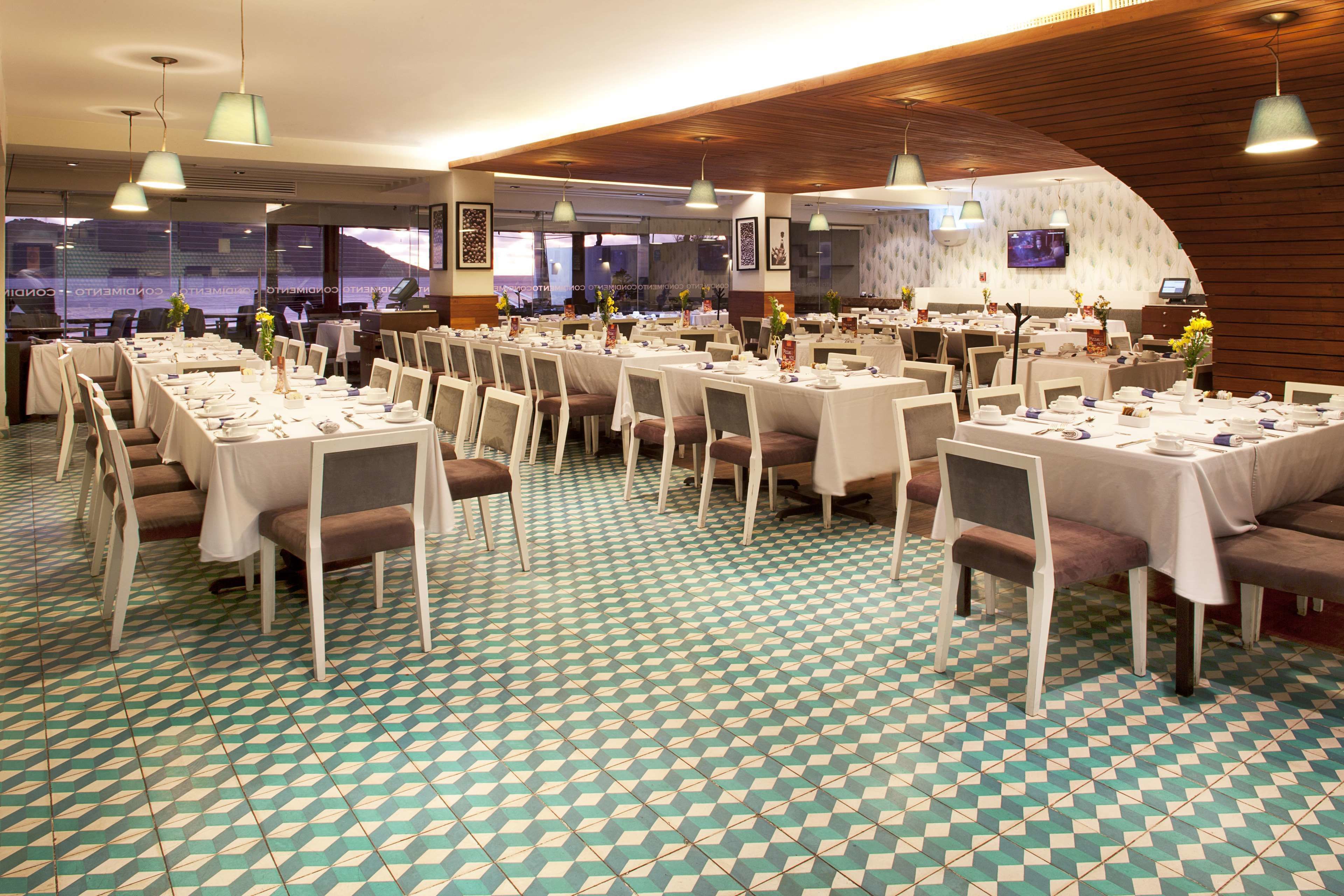 En restaurant med flere borde og stole, et mønstret gulv og hængende lamper.