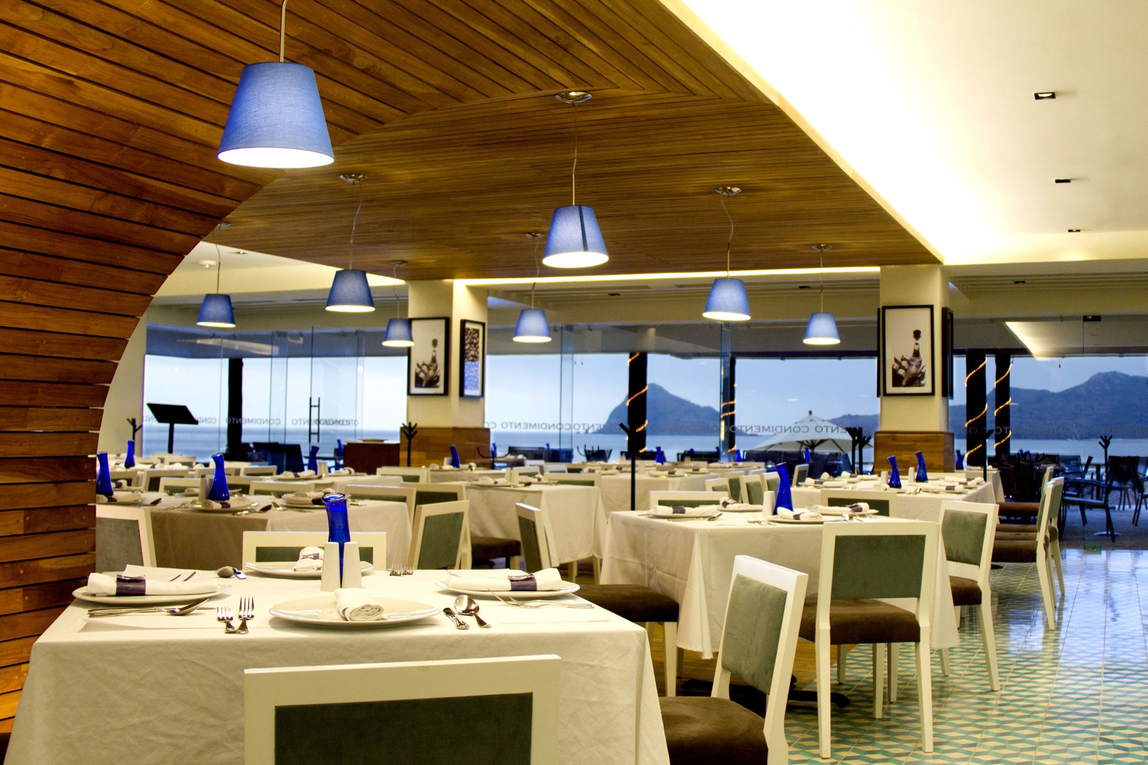 A restaurant with multiple tables, blue hanging lights, and a view of the mountains.