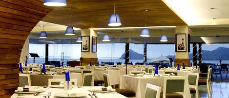 A restaurant with multiple tables, blue hanging lights, and a view of the mountains.