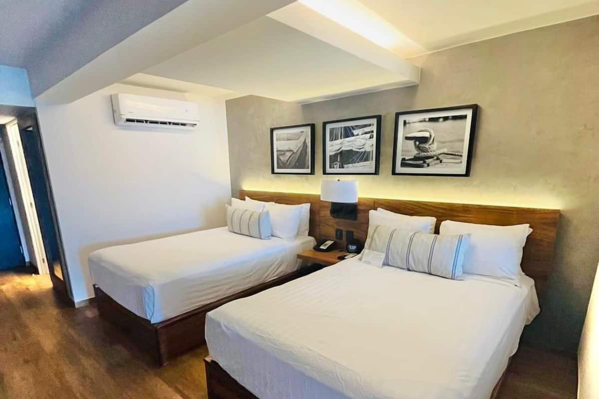 A hotel room with two single beds, a wooden floor, a ceiling fan, and framed pictures on the wall.